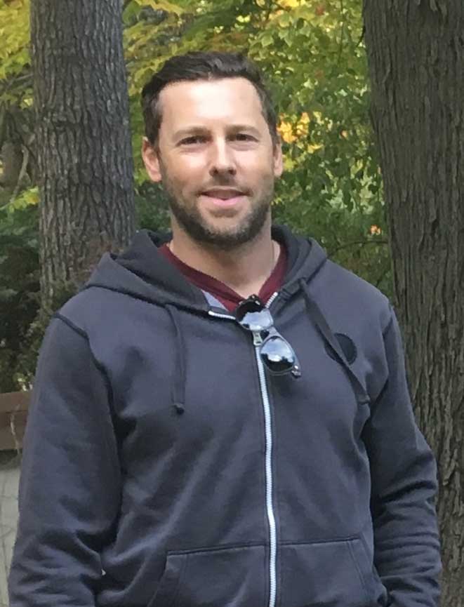 man wearing hoodie standing in front of trees