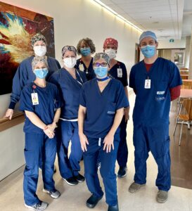 A group of seven OR nurses and doctors in scrubs, caps and masks posing for a picture